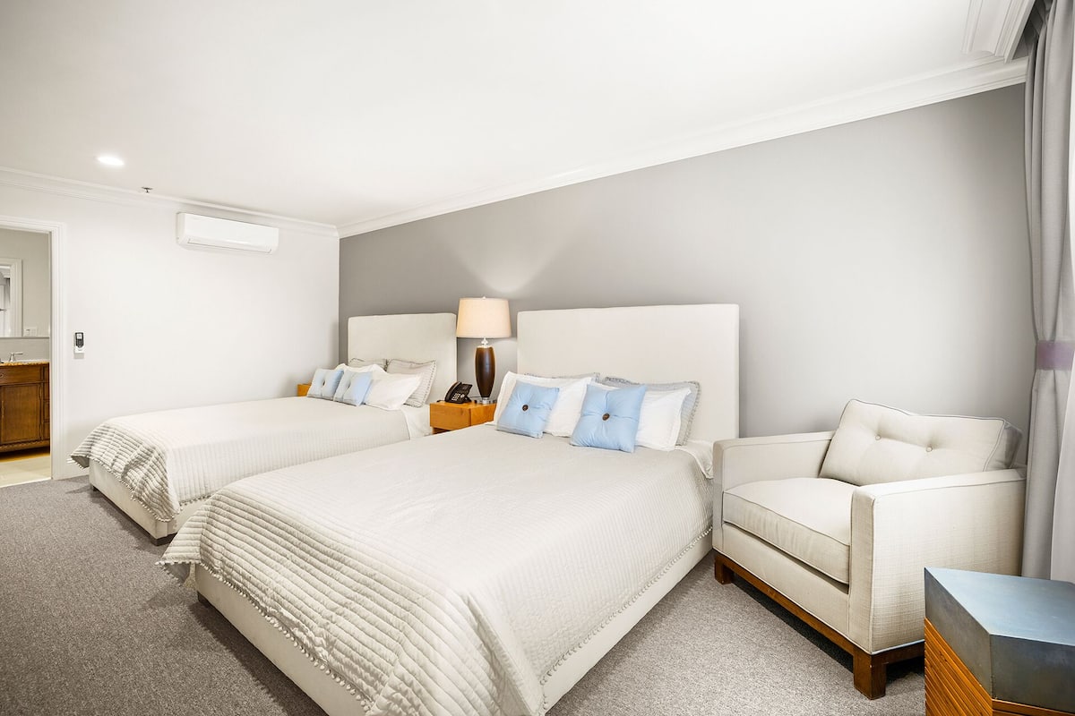 A hotel room with two beds, a sofa, a bedside table with a lamp, and a small table with a phone.