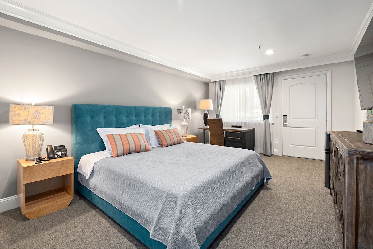 A hotel room with a large bed, a wooden nightstand, a desk, and a wardrobe.