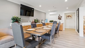 A modern dining area with a wooden table, grey upholstered chairs, and a flat-screen TV mounted on the wall. - Hotel Huntington (Duarte)