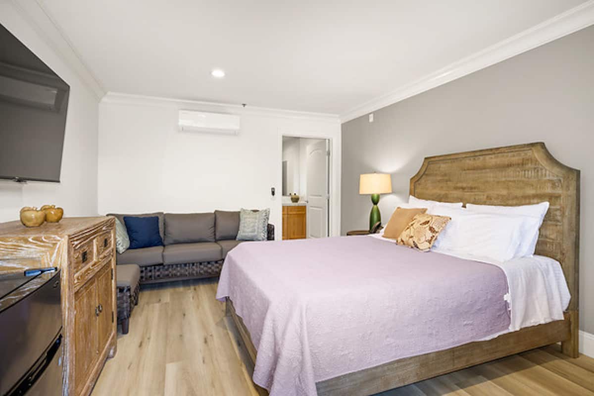 A bedroom with a bed, a sofa, a wooden dresser, and a television on the wall.