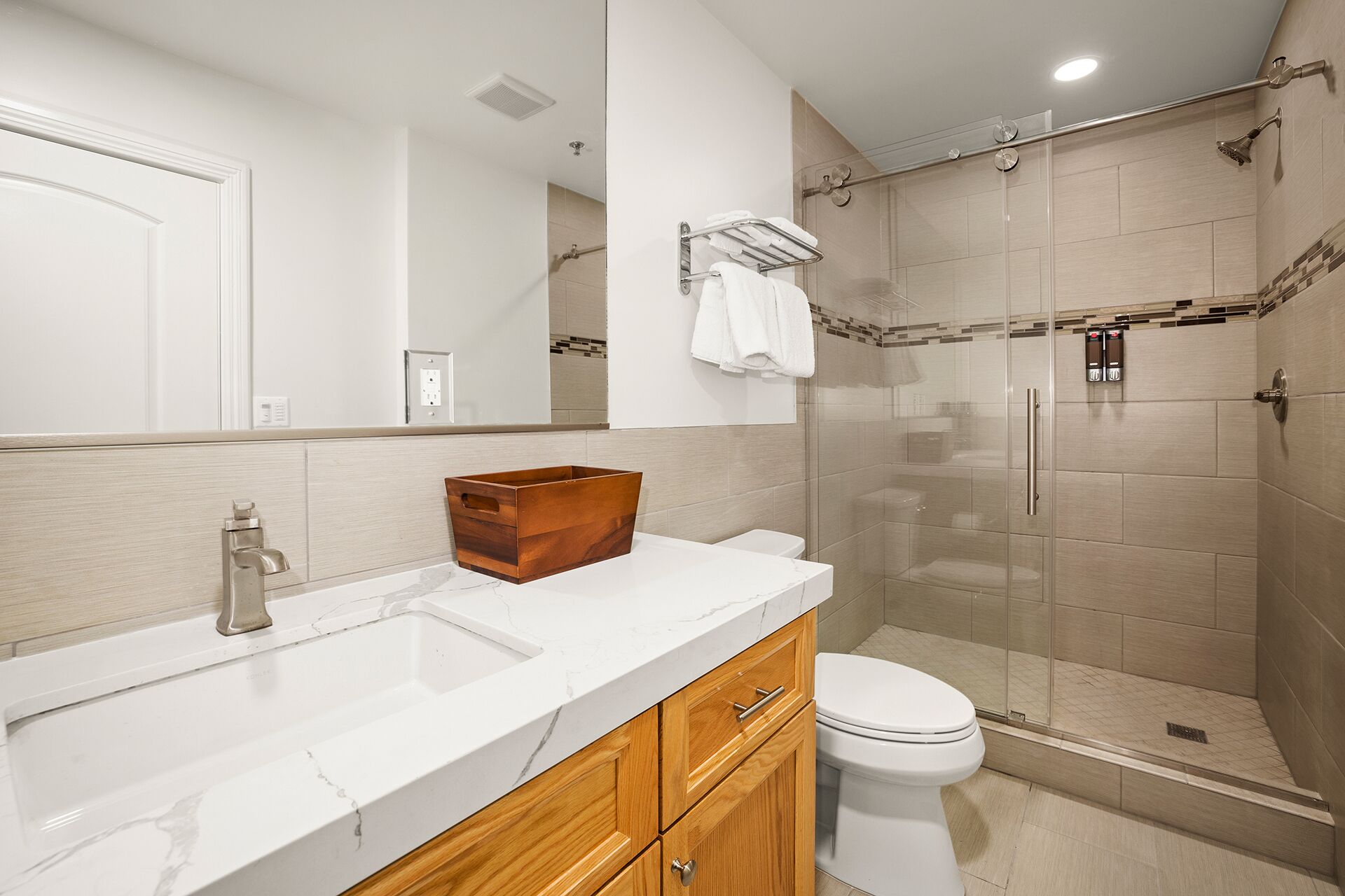 A modern bathroom with a marble sink, wooden cabinets, a glass shower enclosure, and a toilet.
