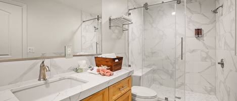Un baño moderno con un lavabo de mármol, armarios de madera, una cabina de ducha de cristal y un inodoro.