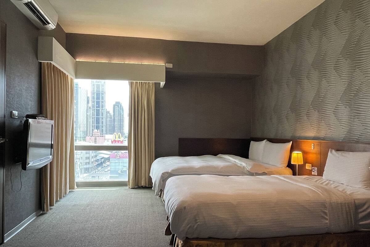 Een hotelkamer met twee bedden, een televisie en uitzicht op een stadsbeeld.