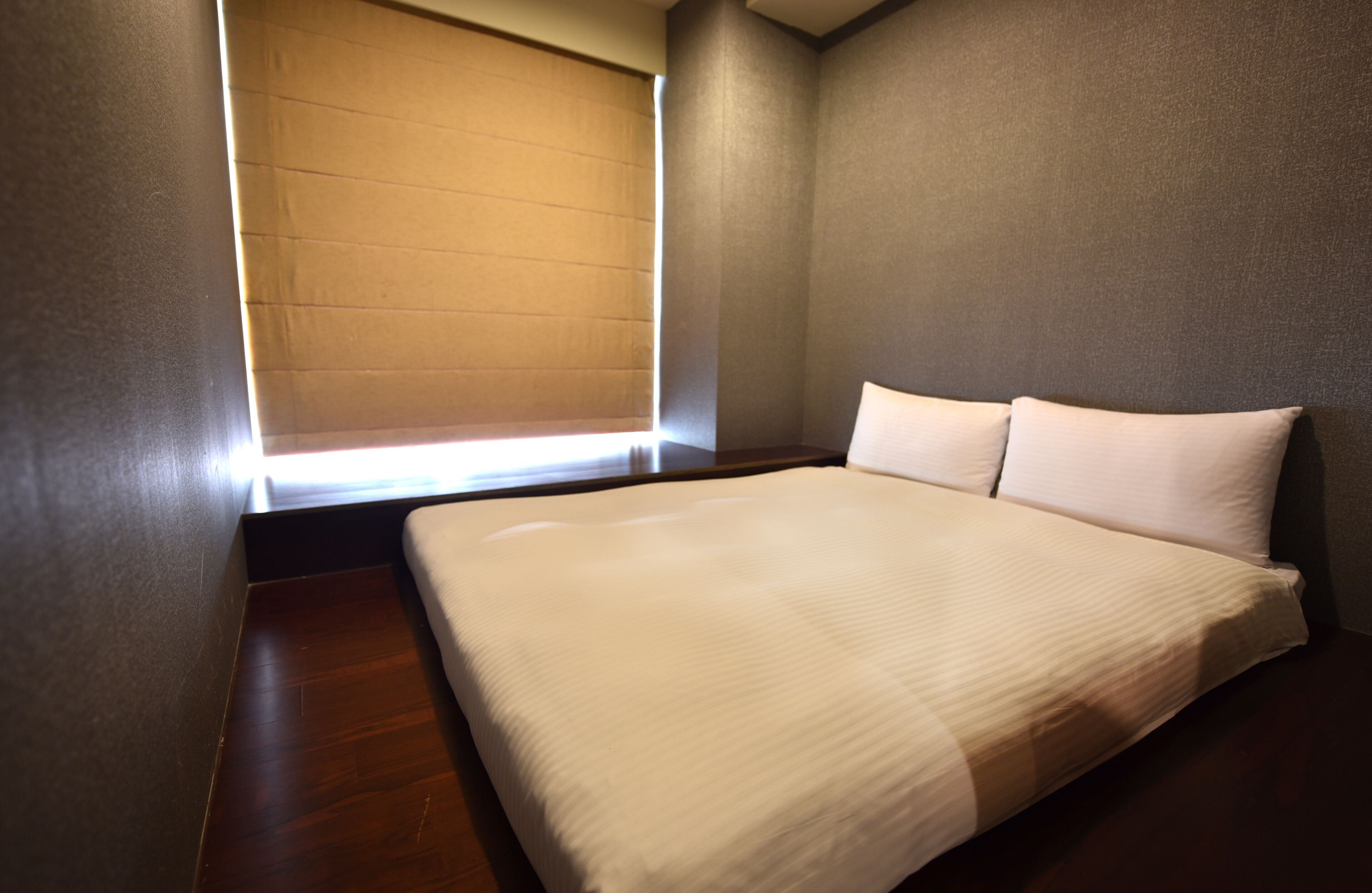 Un dormitorio con una cama grande, una ventana con persianas y suelo de madera.