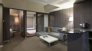 Una habitación de hotel moderna con un sofá, una mesita de centro, una pequeña cocina y un baño visible a través de una puerta abierta.