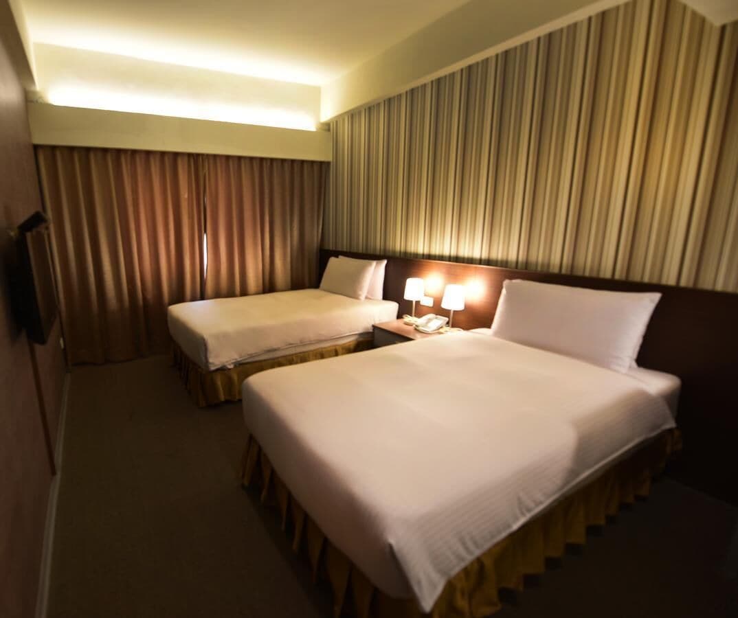 Une chambre d’hôtel avec deux lits, une table de chevet avec des lampes et un rideau.