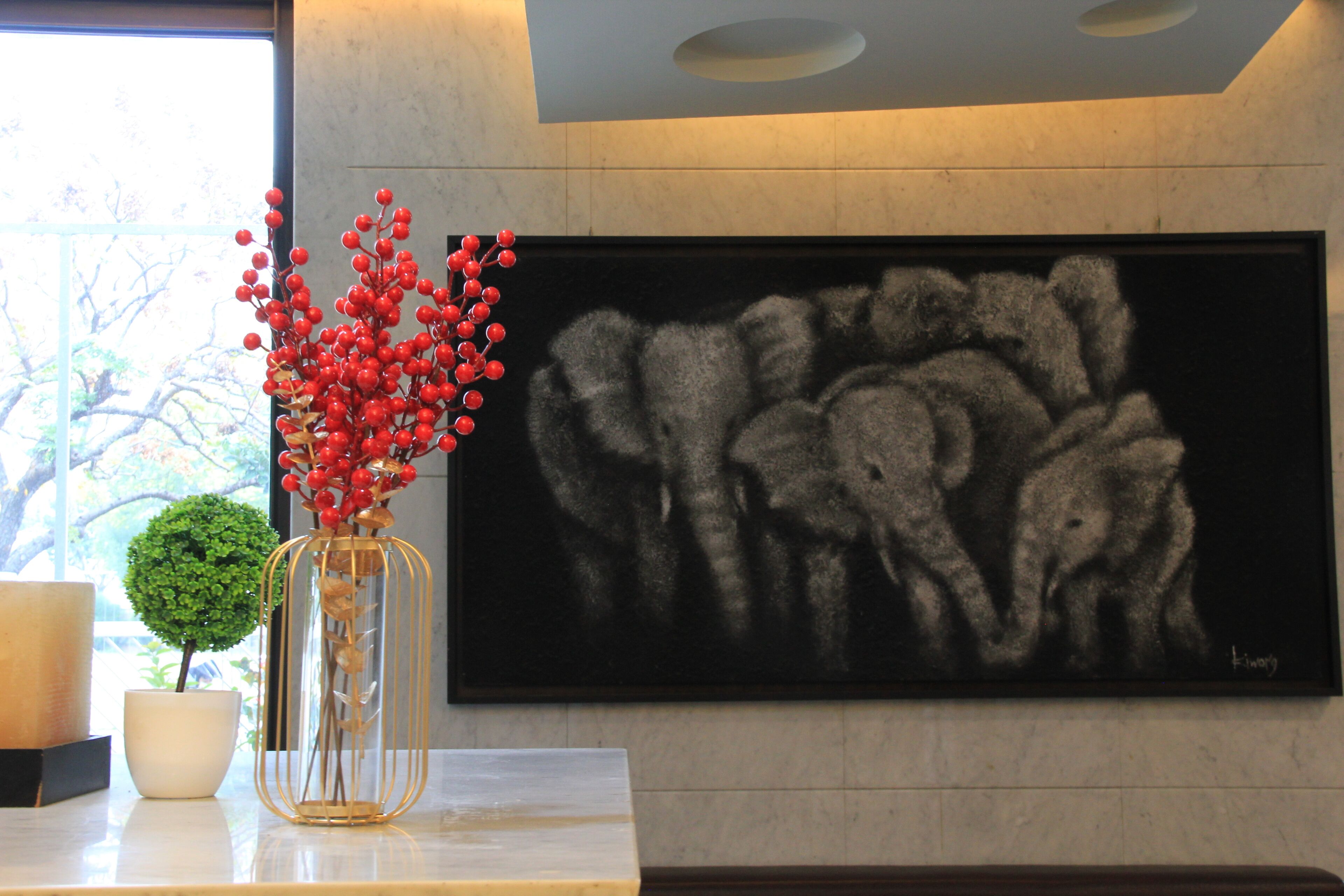A modern interior with a large abstract painting, a clear vase with red berries, and a small potted plant.