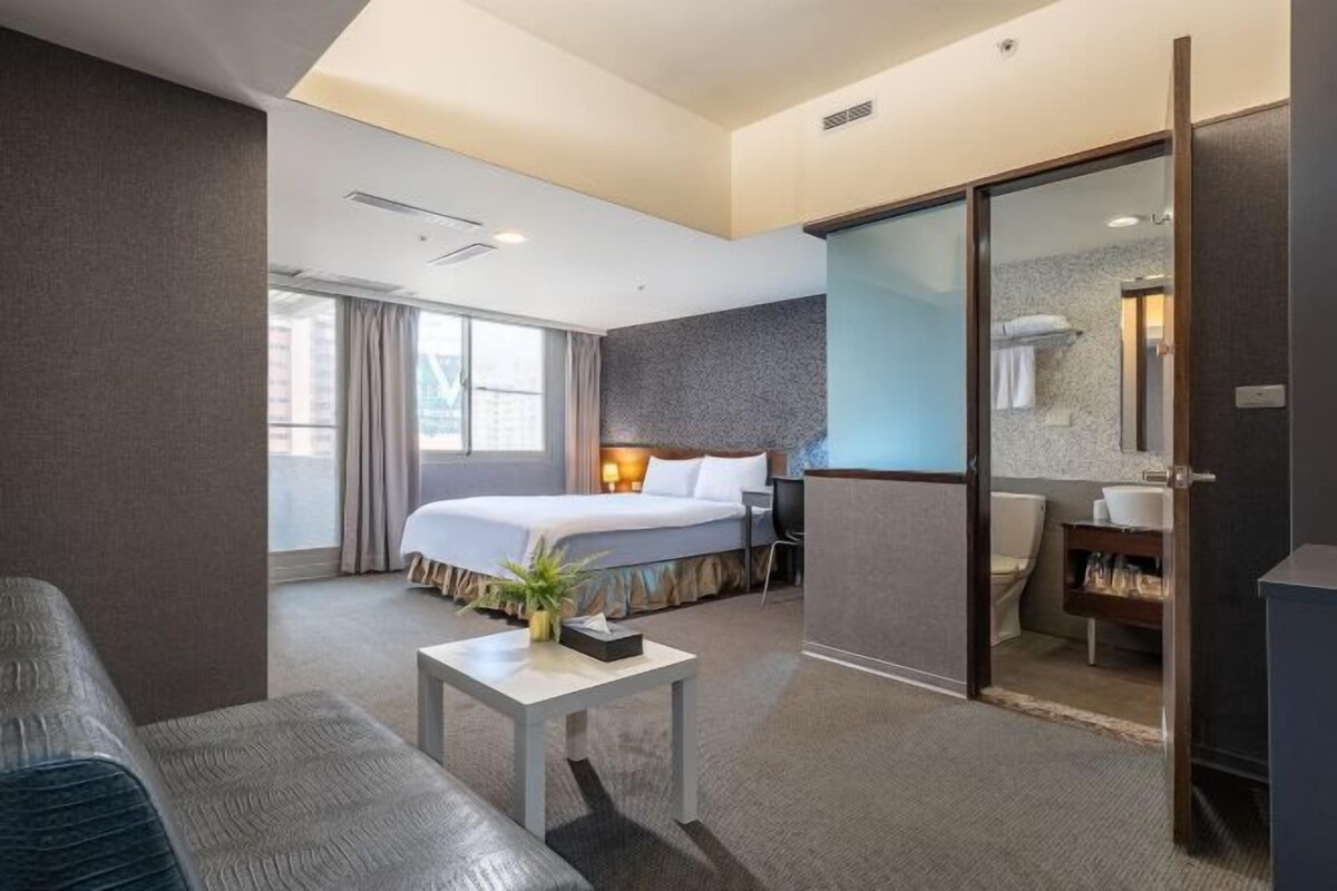 Een hotelkamer met een bed, een bureau, een stoel, een badkamer en uitzicht op de stad.