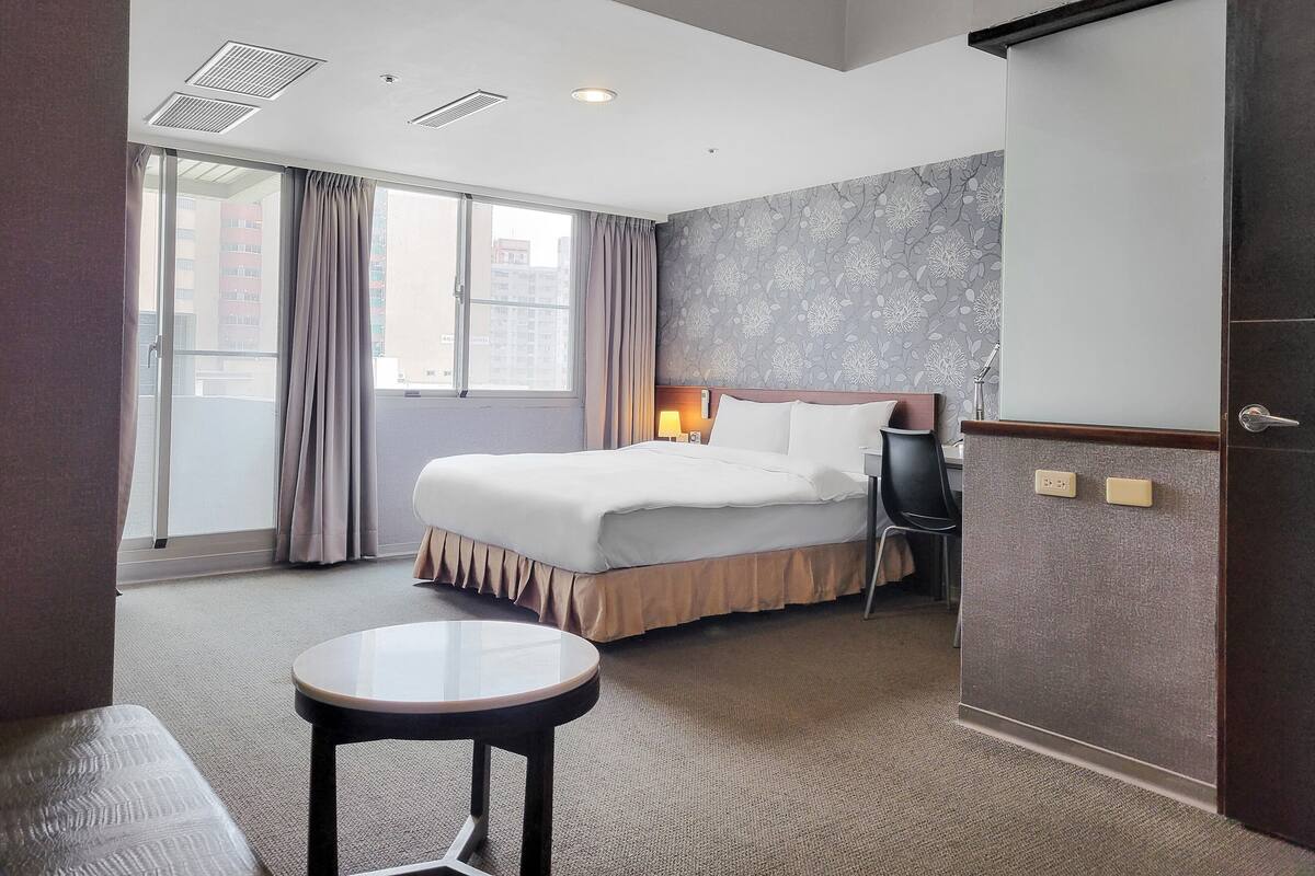 Een hotelkamer met een bed, een bureau, een stoel, een klein tafeltje en een garderobe.