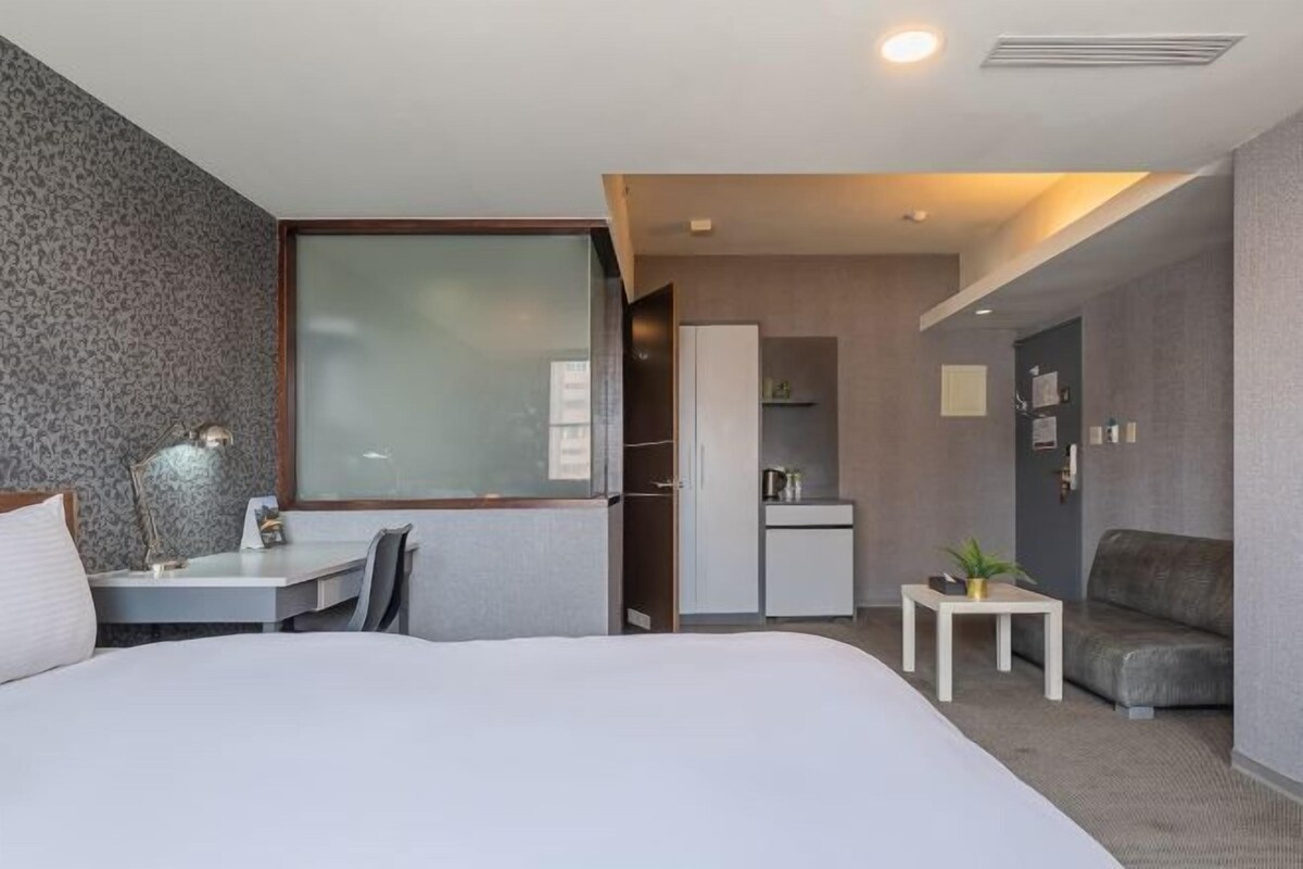 Camera d'albergo moderna con un letto grande, una scrivania, una sedia, un tavolino con una pianta e un divano.