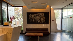 Un vestíbulo moderno con un mostrador de recepción de mármol, un banco, un cuadro abstracto de gran tamaño y un muro de cristal con vistas a árboles.