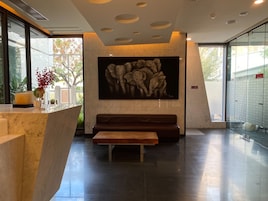 A modern lobby with a marble reception desk, a bench, a large abstract painting, and a glass wall with a view of trees.