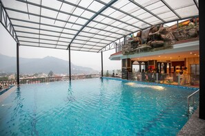 Una piscina interior con techo de cristal, una cascada y vistas a montañas distantes.