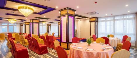 A banquet hall with round tables, red and yellow chairs, and chandeliers.