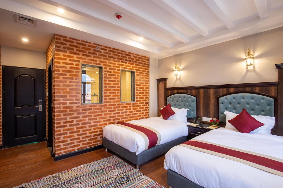 A hotel room with two beds, a brick wall, wooden ceiling beams, and a patterned rug.
