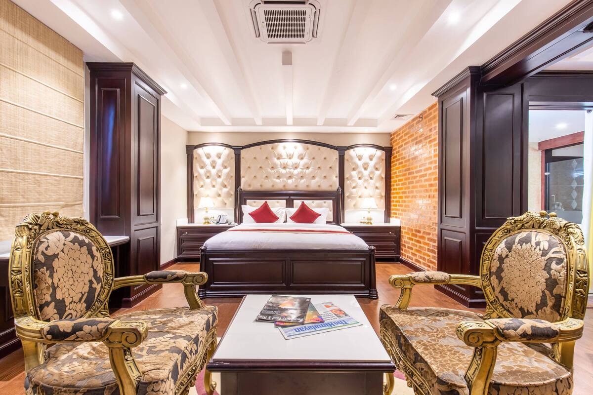 A spacious bedroom with a large bed, two ornate chairs, a coffee table, and a brick accent wall.