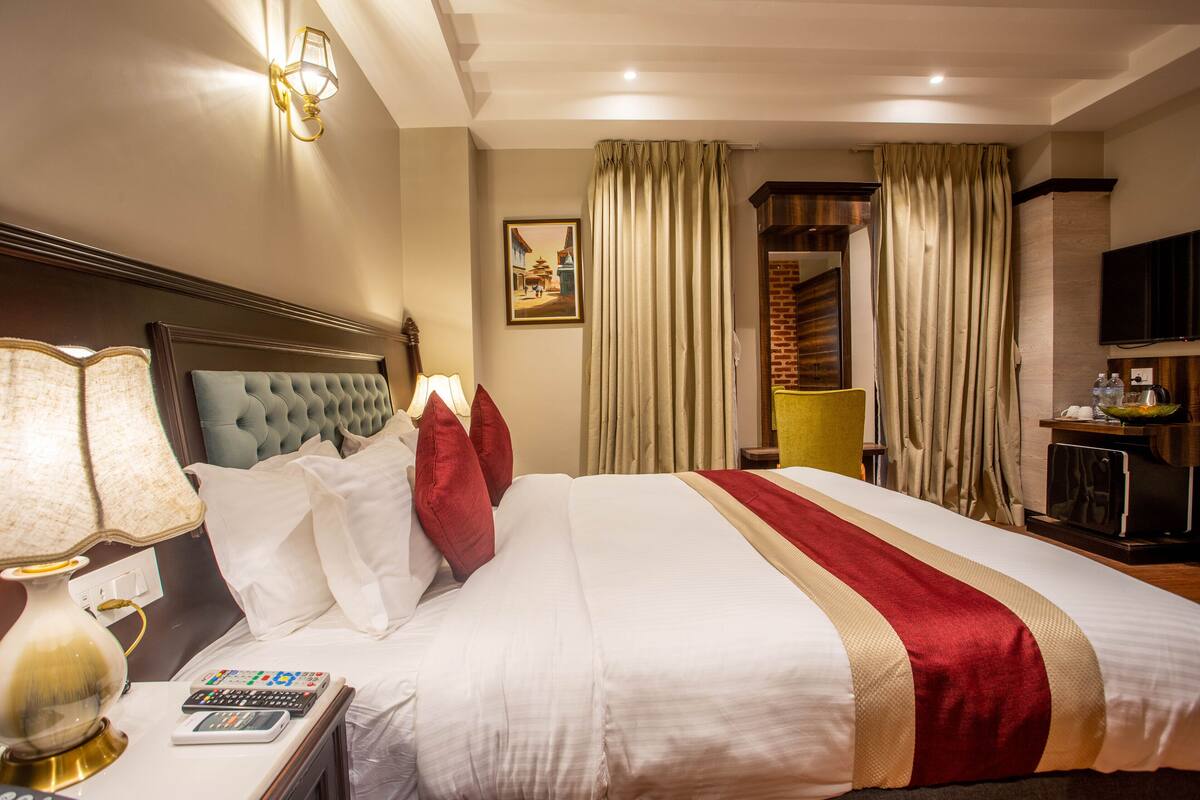 A hotel room with a large bed, a bedside lamp, a flat-screen TV, and a painting on the wall.
