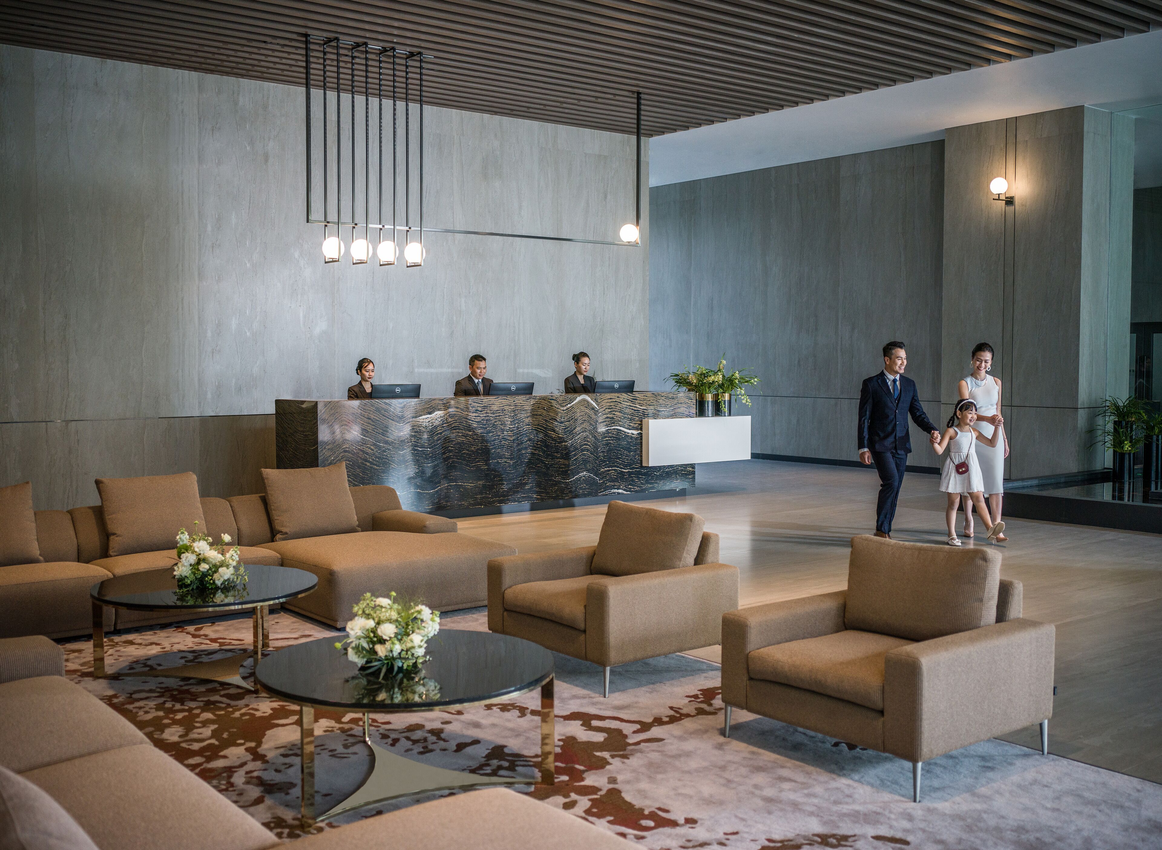 A modern lobby with sofas, a reception desk, and a family walking through.