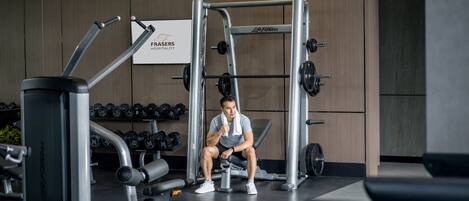 A gym with weightlifting equipment, dumbbells, and a sign for 'Frasers Hospitality'.