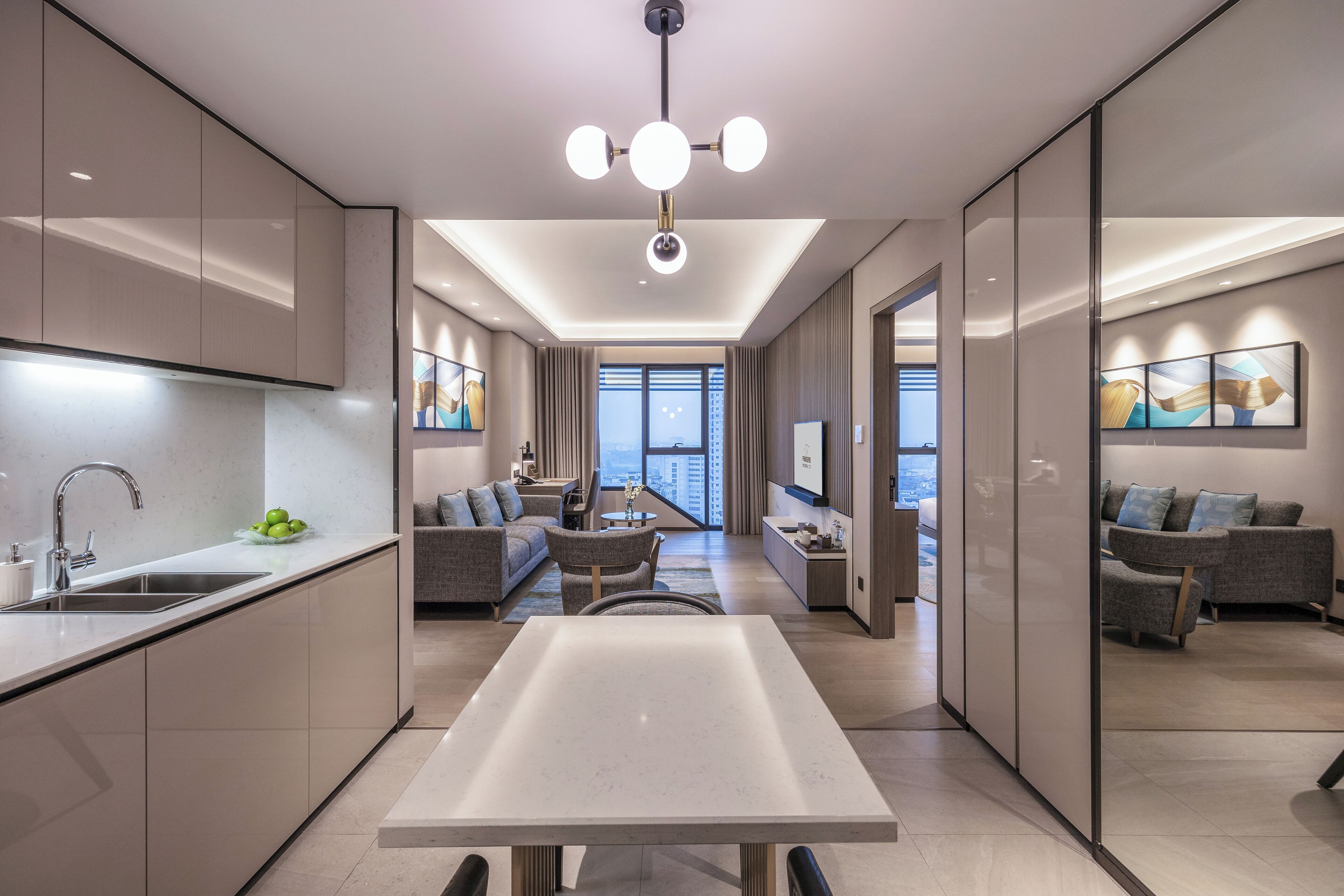 A modern kitchen with a central island, a dining area with a long table, and a living space with sofas and a TV.