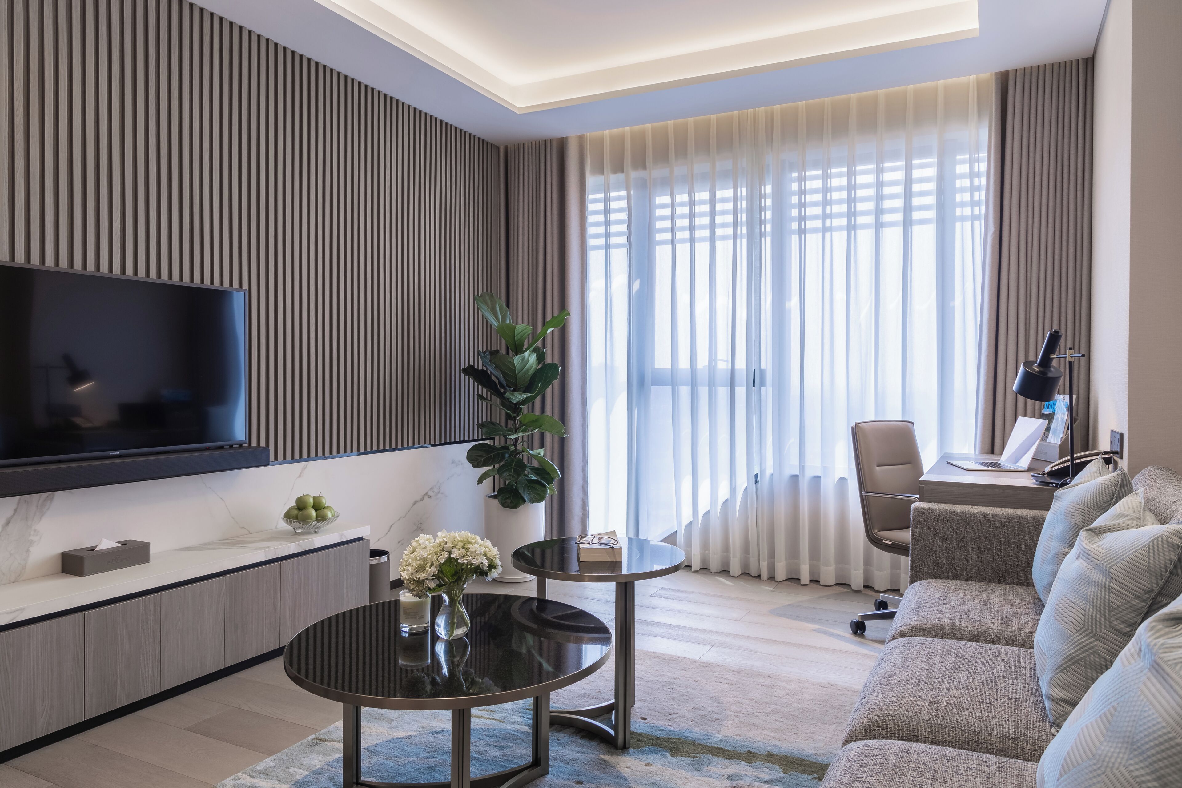 A modern living room with a flat-screen TV, a round coffee table, a sofa, and a chair.