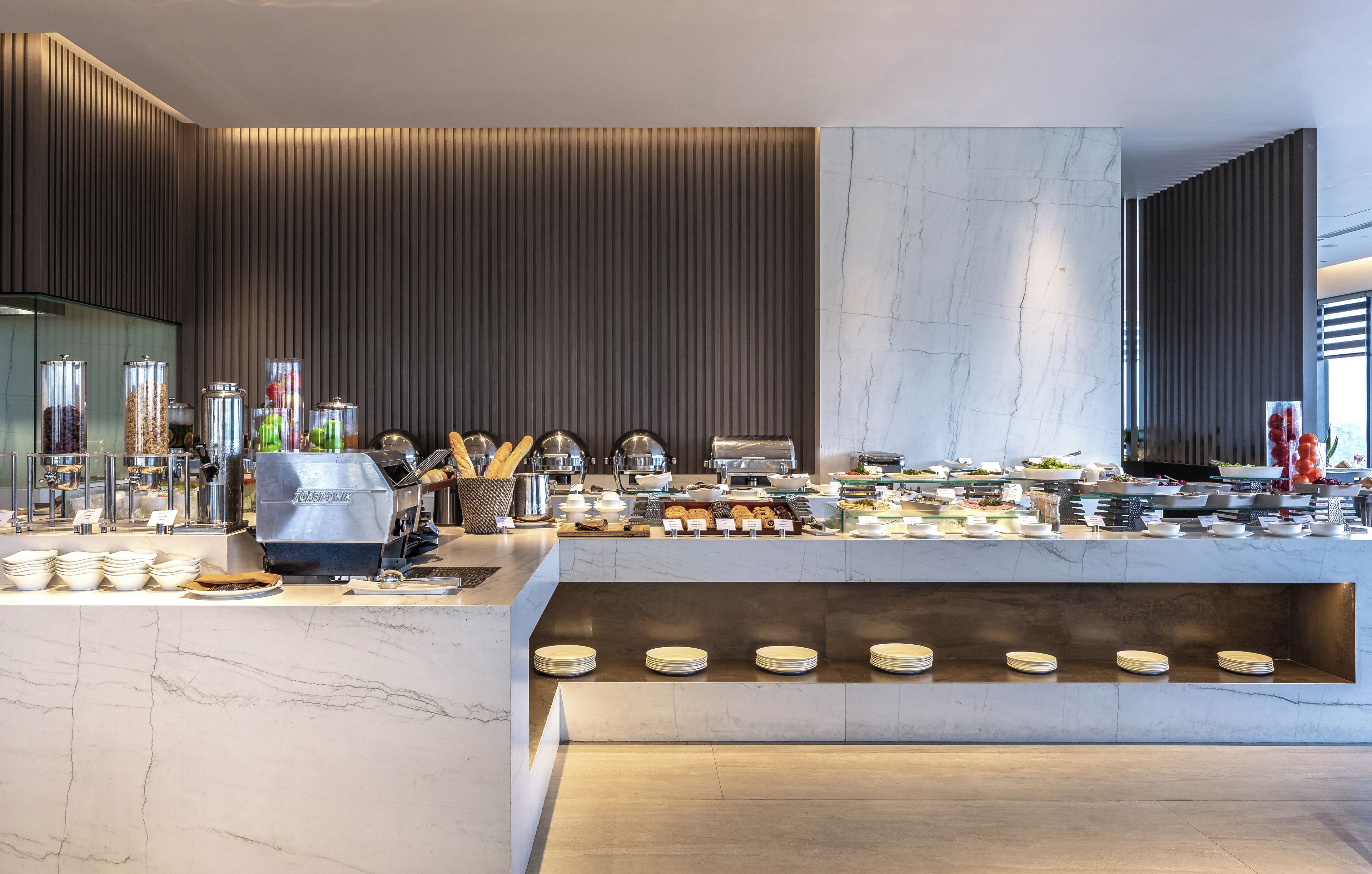 A modern buffet setup with a variety of food items, a coffee machine, and neatly arranged plates.
