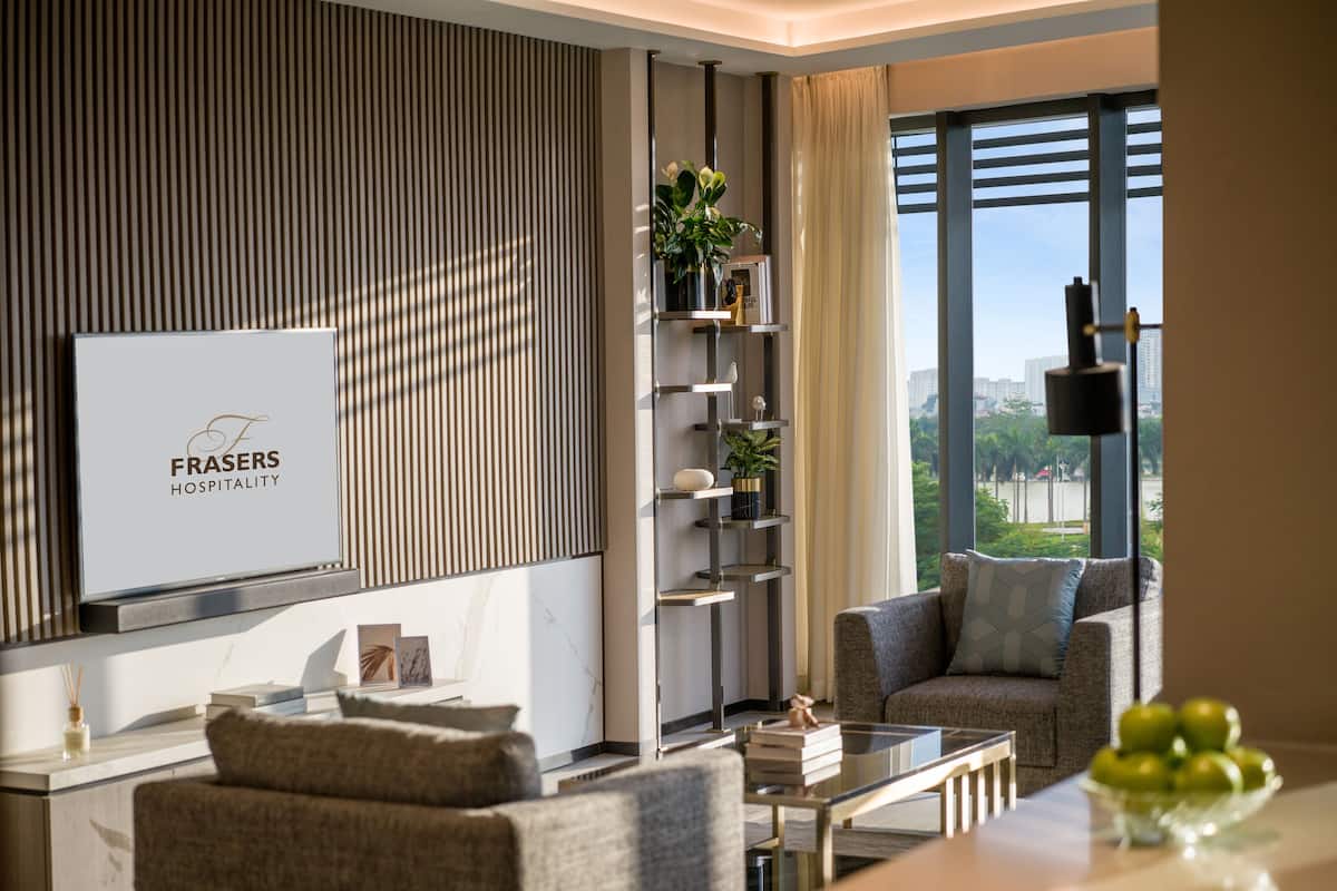 A modern living room with a sofa, a coffee table, and a TV screen displaying 'Frasers Hospitality'.