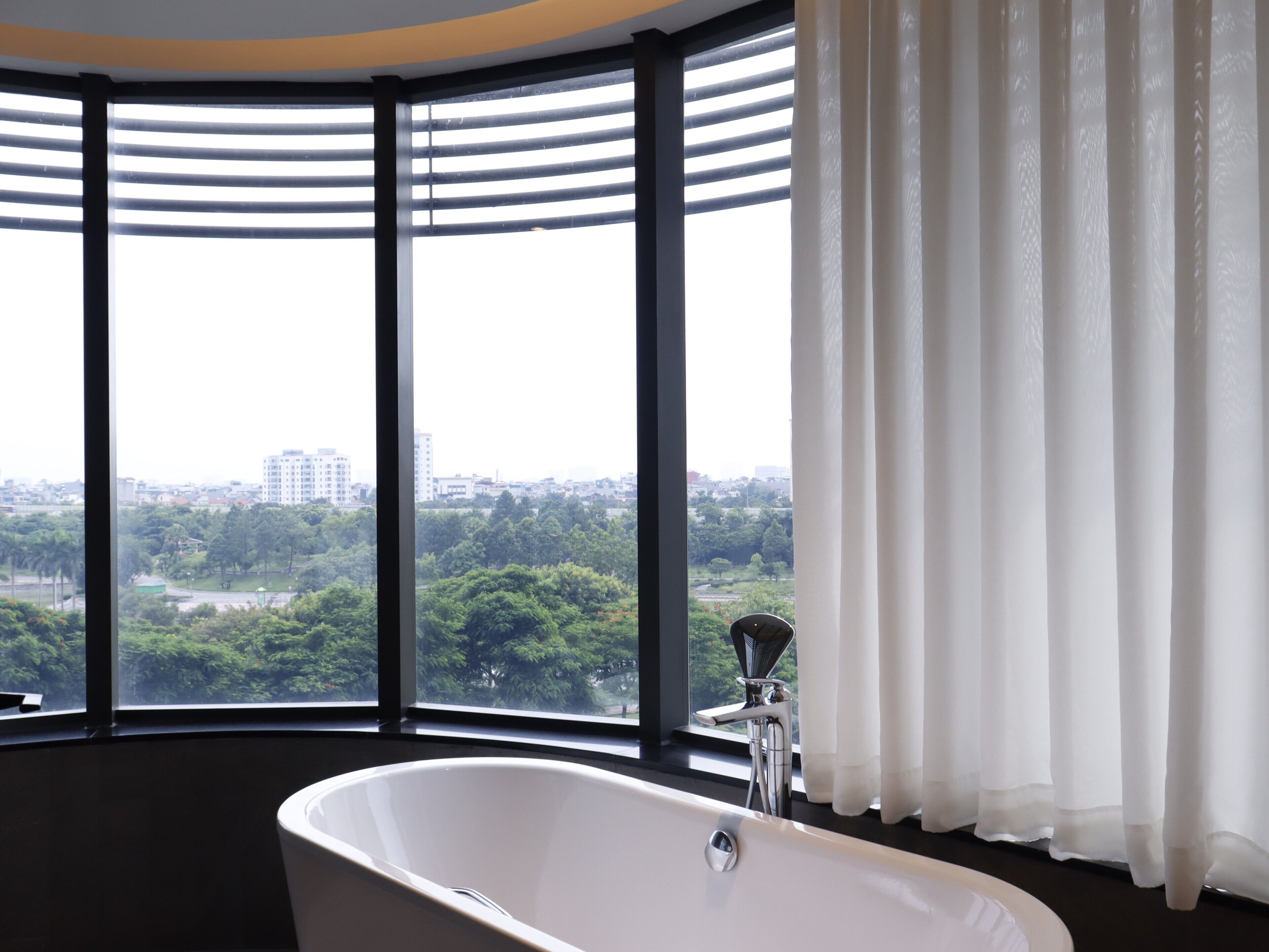 A modern bathroom with a freestanding bathtub, large windows, and a view of a cityscape.