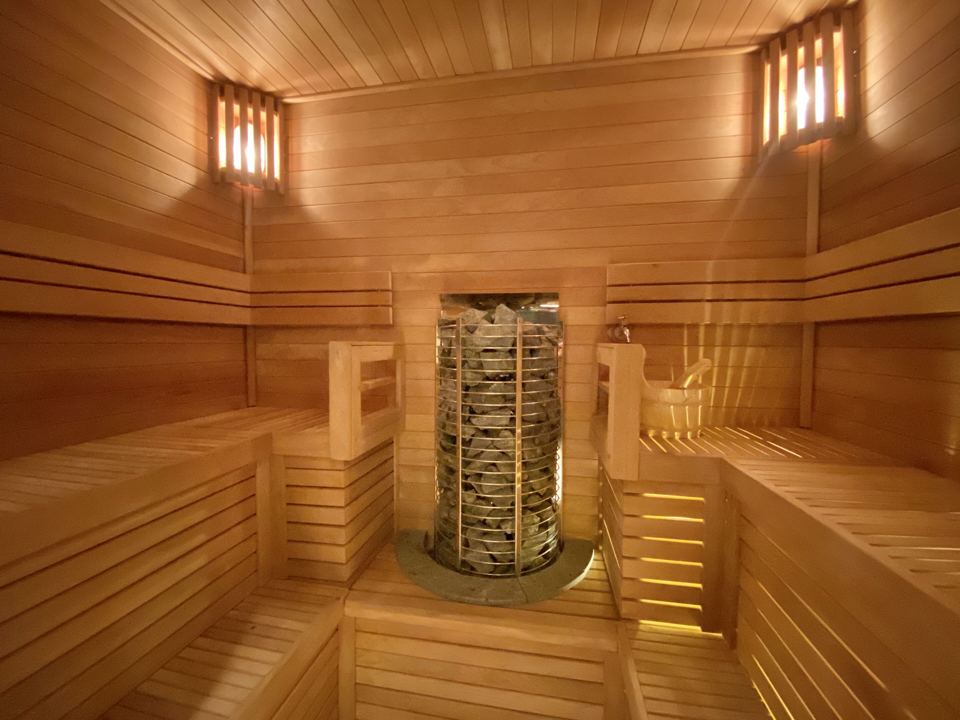 Eine Sauna mit Holzwänden und -bänken, einer zentralen Steinanlage und einem kleinen Waschbecken.