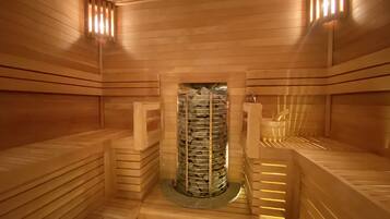 Eine Sauna mit Holzwänden und -bänken, einer zentralen Steinanlage und einem kleinen Waschbecken.