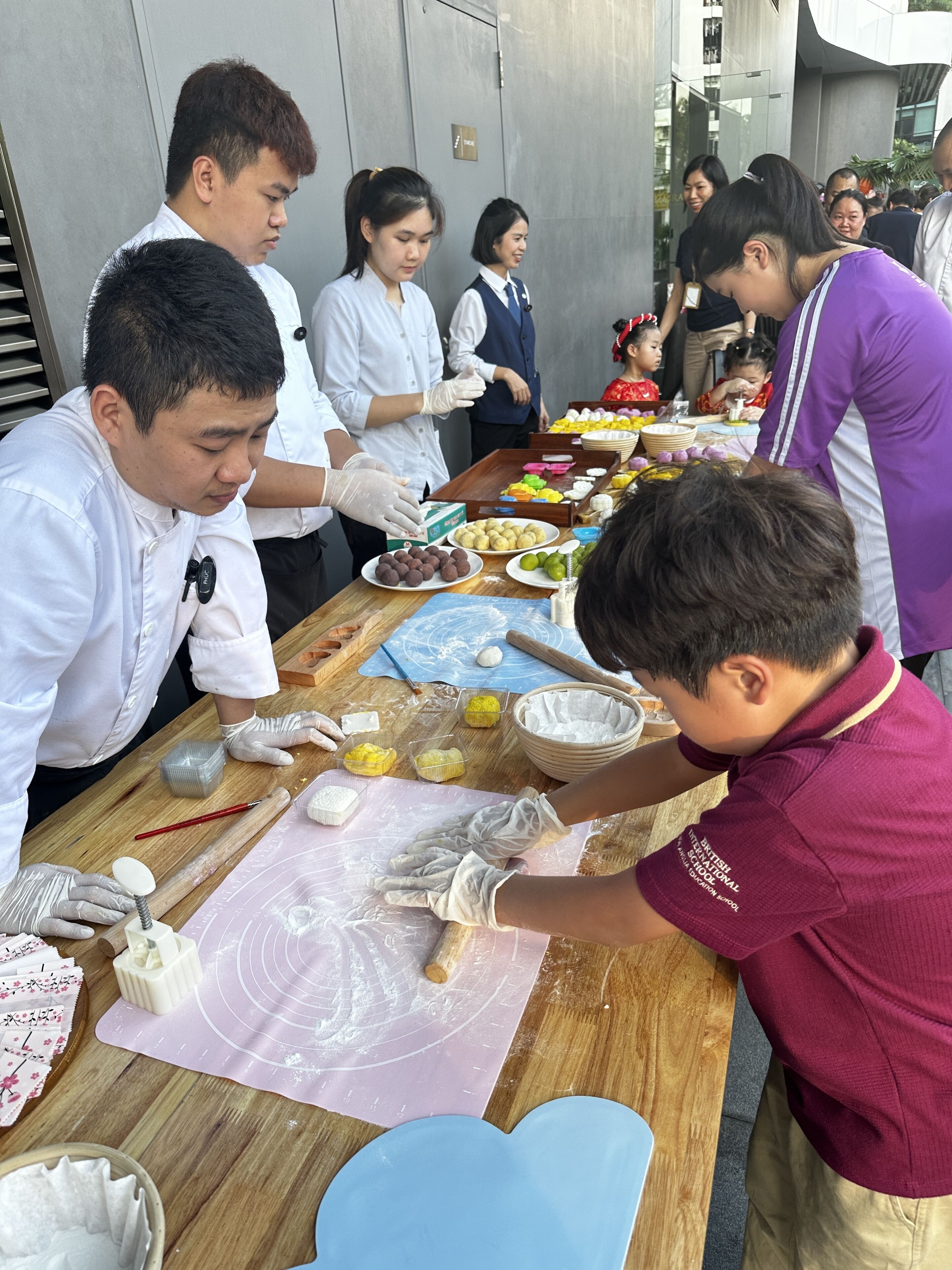 A group of people engaged in a food preparation activity outdoors, with a variety of food items and utensils on a wooden table.