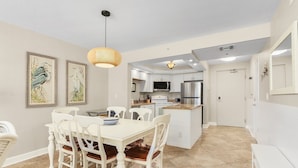Une cuisine moderne avec des meubles blancs, un îlot central et un coin repas comprenant une table et des chaises blanches.