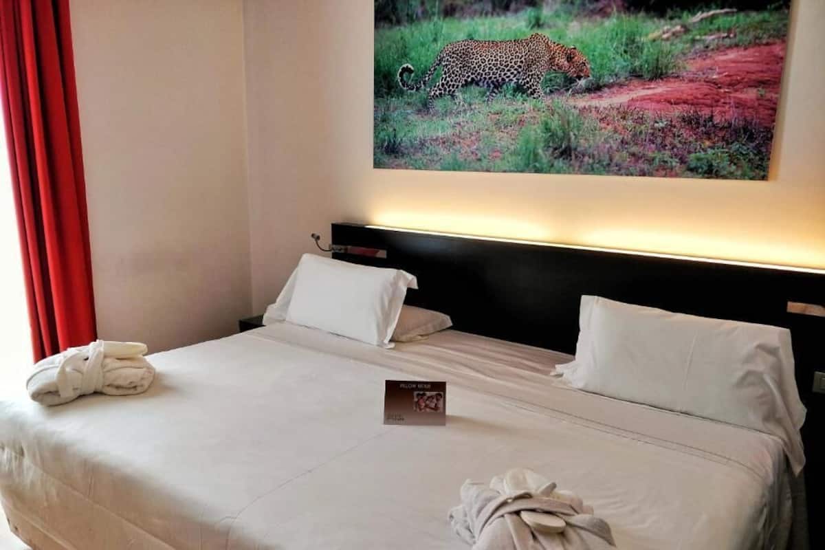 A hotel room with a bed, white pillows, a folded towel, and a framed picture of a leopard on the wall.