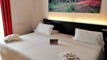 A hotel room with a bed, white pillows, a folded towel, and a framed picture of a leopard on the wall.