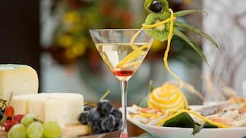 A martini glass with a kiwi slice and a yellow fruit garnish, surrounded by cheese, grapes, and a plate of food.