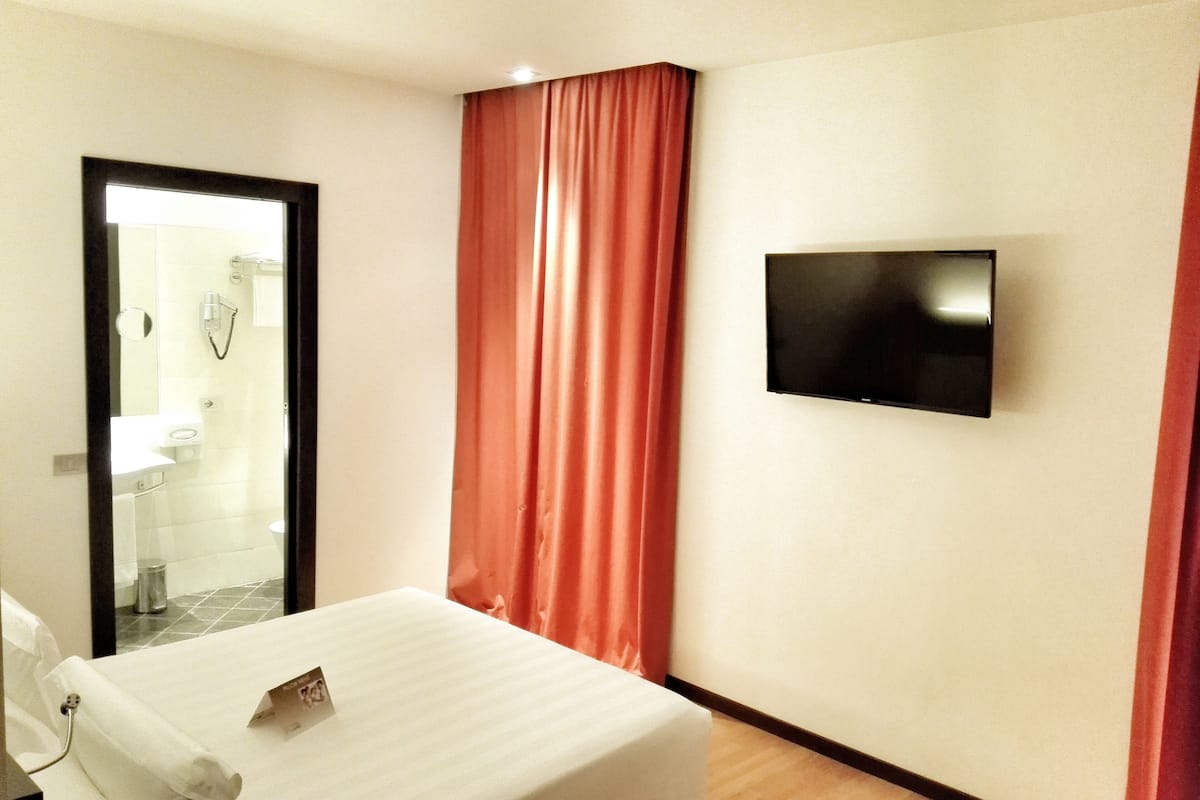 A hotel room with a bed, a television mounted on the wall, and a bathroom visible through an open door.