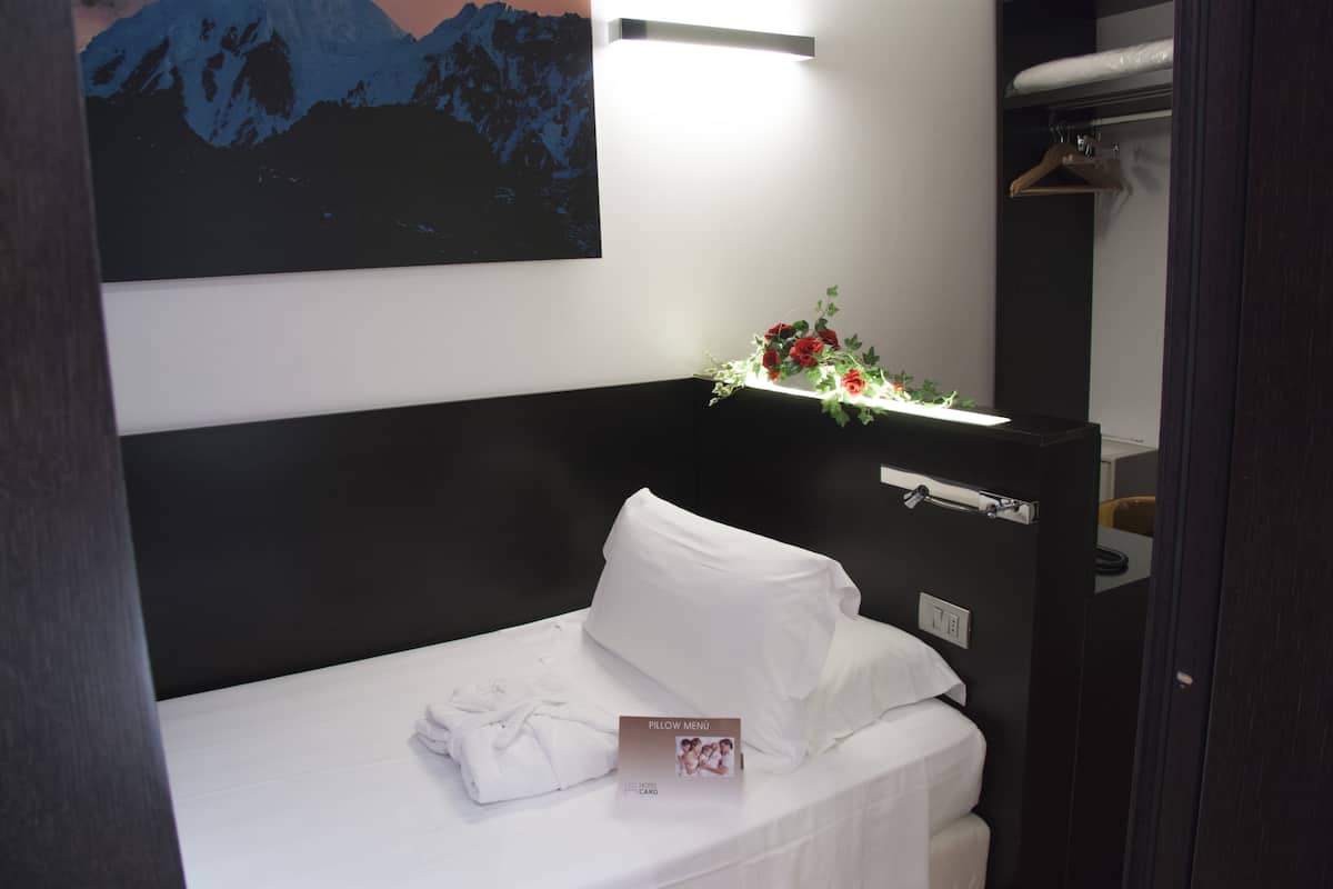 A neatly made bed with white linens, a pillow menu, and a small floral arrangement on a bedside table.