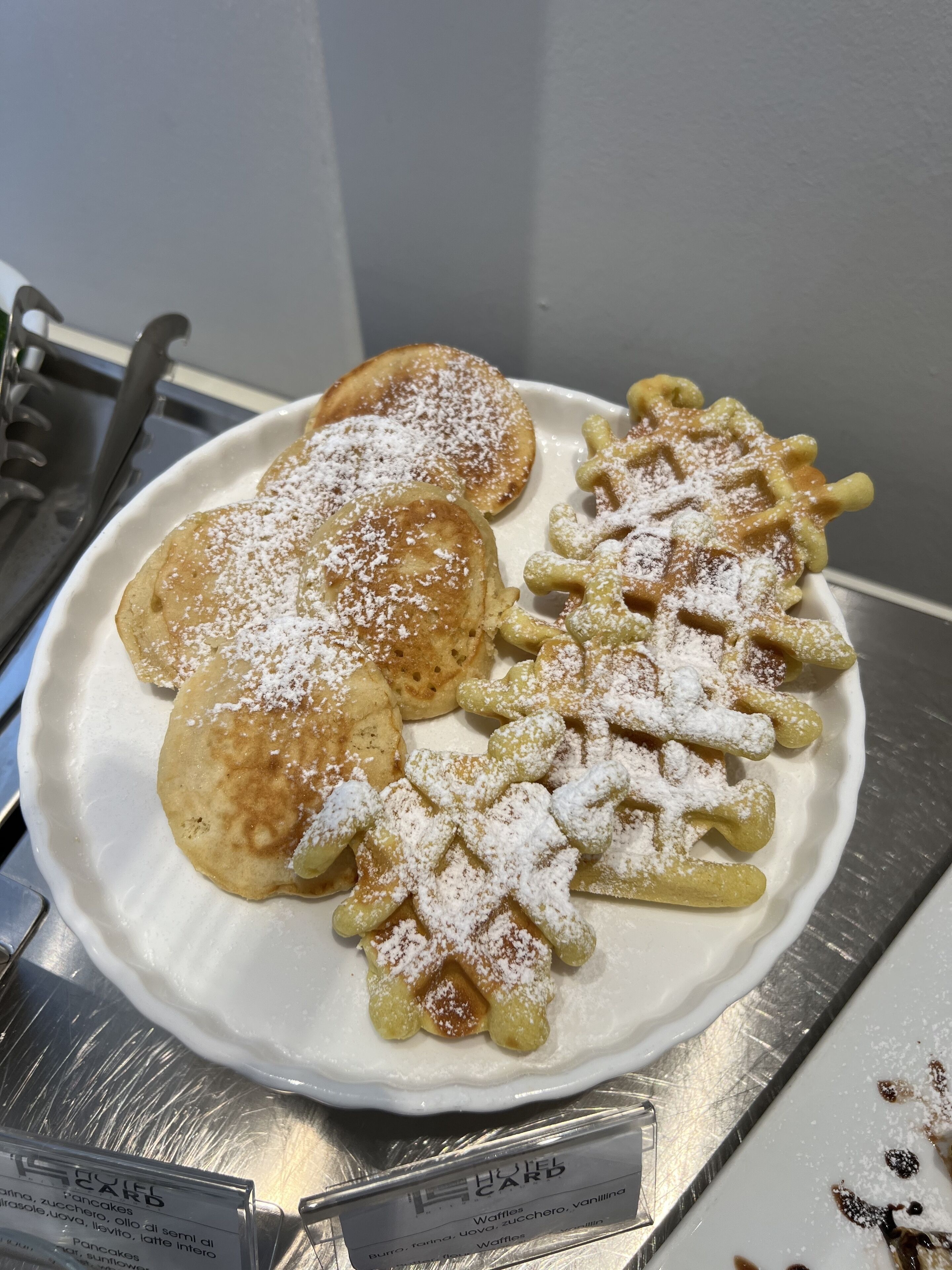 A plate of pancakes and waffles with powdered sugar, placed on a white plate.