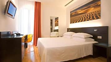 A hotel room with a large bed, a desk with a chair, a television, and a painting of a desert landscape.