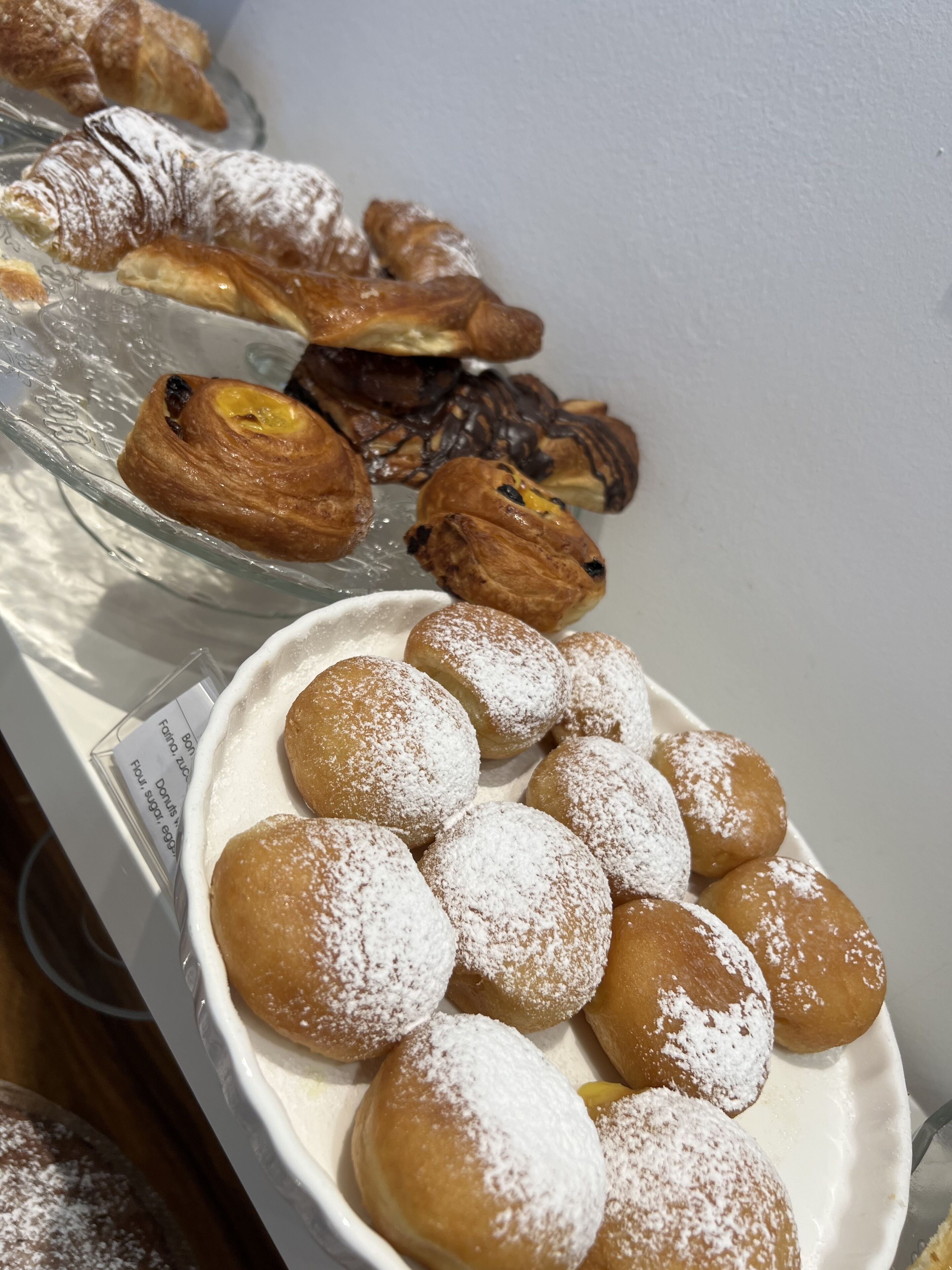 A variety of pastries including croissants and powdered doughnuts on display.