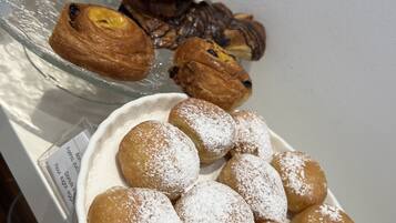 A variety of pastries including croissants and powdered doughnuts on display.
