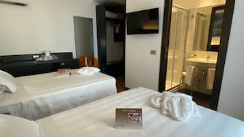Une chambre d’hôtel avec deux lits, une table de chevet, une télévision, un miroir et une salle de bain visible à travers une porte ouverte.