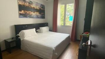 Een slaapkamer met een bed, nachtkastje, schilderij aan de muur en een raam met gordijnen.