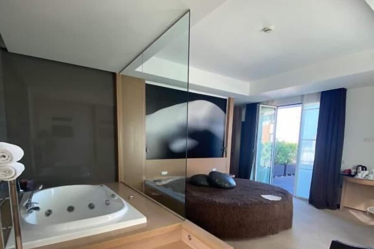A modern bathroom with a freestanding bathtub, a large mirror, and a seating area with a bench.
