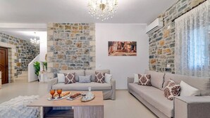 A living room with stone walls, two sofas, a coffee table, and a chandelier. - Villa Orestis - Faraggi Villas (Zoniana)