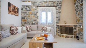 A living room with a stone wall, a sofa, a coffee table with snacks, and a fireplace. - Villa Orestis - Faraggi Villas (Zoniana)