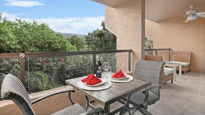 Ein Balkon mit Tisch für zwei Personen, einer Weinflasche und einem Glas. Es gibt Korbstühle und einen Deckenventilator.