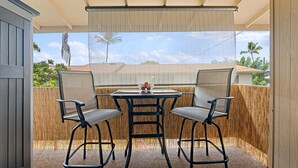 Un patio exterior con una mesa y dos sillas, un cerramiento tejido y vistas a palmeras y casas.