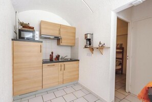Cocina pequeña con armarios de madera, un microondas y una cafetera sobre una repisa.