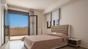 A bedroom with a bed, a nightstand, a window with blinds, and an open sliding door to a balcony.